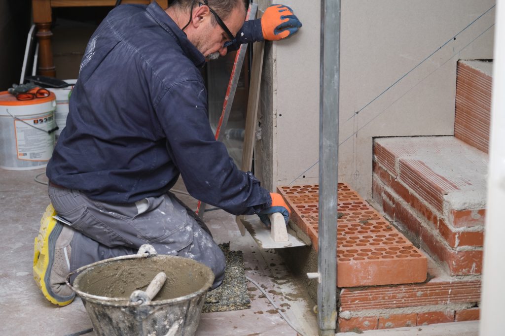 Bricklayer building a brick staircase in a home interior.